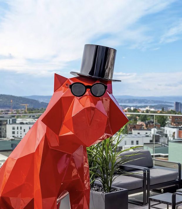 En slående rød løvestatue med solbriller og topplue, som kombinerer eleganse med en leken vri.